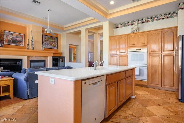 kitchen featuring white appliances, sink, a kitchen island with sink, ceiling fan, and light brown cabinets