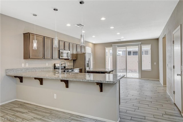 kitchen with decorative light fixtures, a kitchen bar, kitchen peninsula, appliances with stainless steel finishes, and light stone countertops