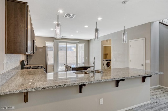 kitchen with hanging light fixtures, range, light stone counters, a breakfast bar, and sink