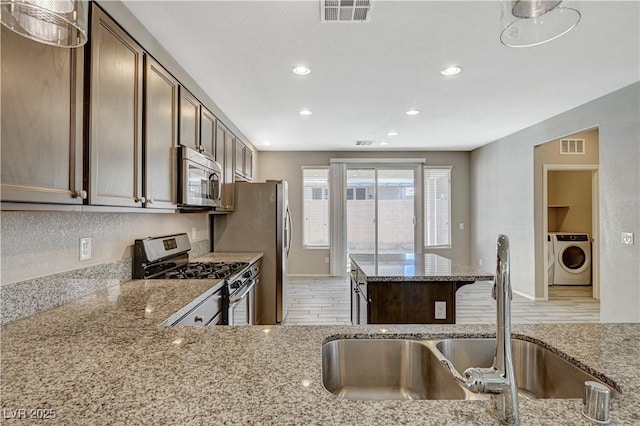 kitchen with washer / dryer, light hardwood / wood-style floors, stainless steel appliances, light stone countertops, and sink