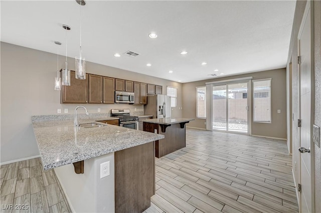 kitchen with decorative light fixtures, a breakfast bar, kitchen peninsula, sink, and stainless steel appliances