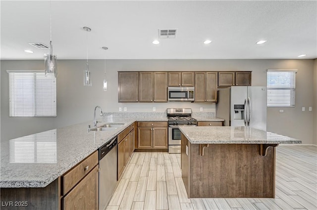 kitchen with decorative light fixtures, stainless steel appliances, sink, light stone counters, and a breakfast bar