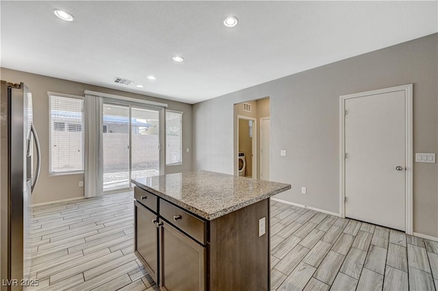 kitchen featuring stainless steel refrigerator with ice dispenser, a kitchen island, dark brown cabinetry, and light stone countertops