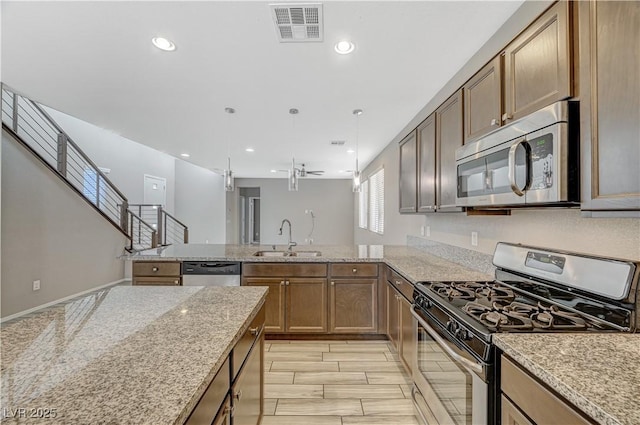 kitchen featuring appliances with stainless steel finishes, decorative light fixtures, sink, ceiling fan, and light stone counters