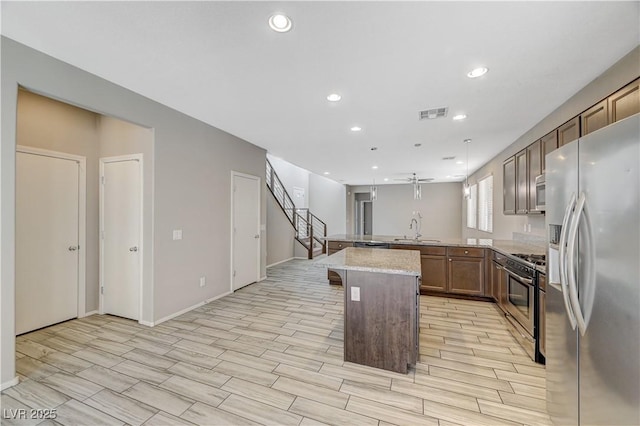 kitchen featuring a breakfast bar area, stainless steel appliances, decorative light fixtures, a kitchen island, and light stone counters