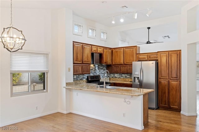 kitchen featuring appliances with stainless steel finishes, pendant lighting, sink, light stone counters, and kitchen peninsula