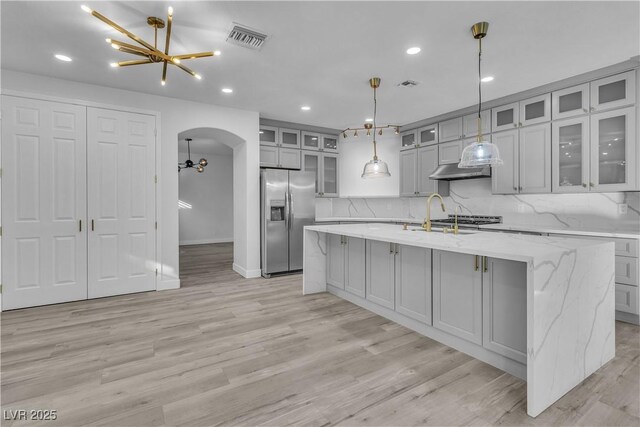 kitchen featuring light stone countertops, a center island with sink, backsplash, and stainless steel refrigerator with ice dispenser