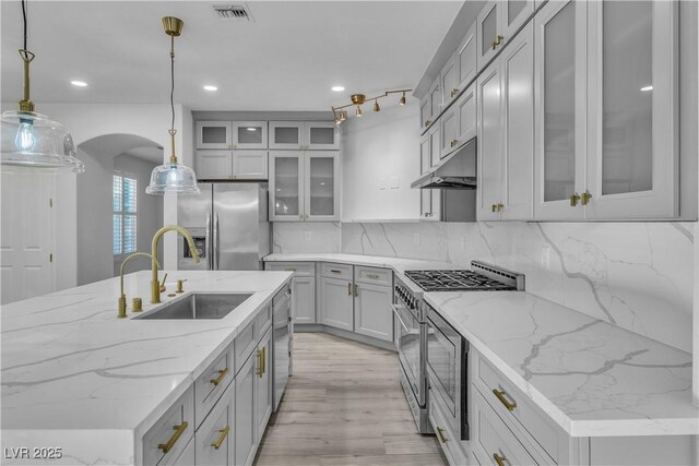 kitchen featuring a kitchen island with sink, hanging light fixtures, stainless steel appliances, sink, and tasteful backsplash