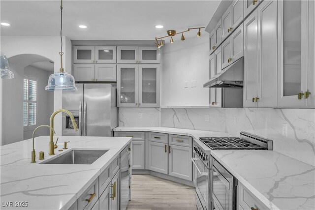 kitchen with hanging light fixtures, stainless steel appliances, light stone countertops, sink, and tasteful backsplash