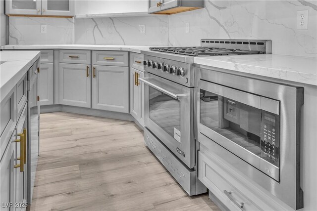 kitchen featuring stainless steel stove, light hardwood / wood-style flooring, light stone countertops, backsplash, and gray cabinets