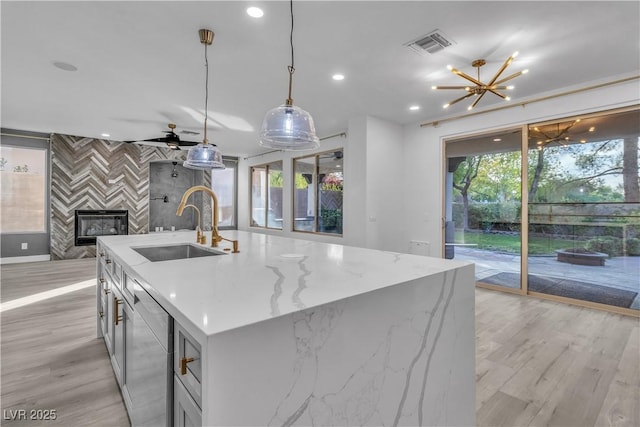 kitchen with a center island with sink, light stone countertops, pendant lighting, sink, and ceiling fan with notable chandelier