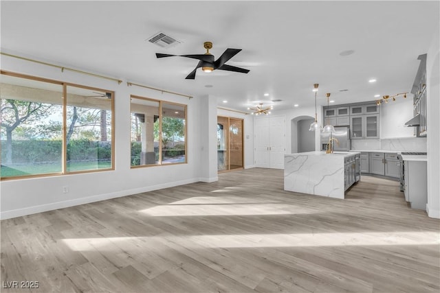 kitchen featuring an island with sink, ceiling fan, light stone counters, light hardwood / wood-style flooring, and decorative light fixtures