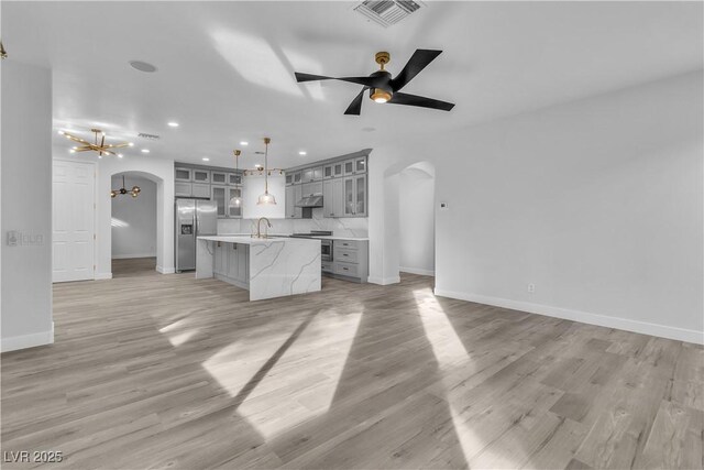 kitchen with gray cabinetry, stainless steel fridge, pendant lighting, a kitchen island, and ceiling fan with notable chandelier