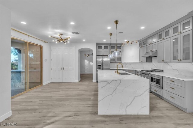 kitchen featuring decorative light fixtures, an island with sink, light stone countertops, and sink