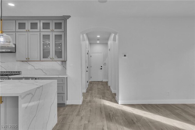 kitchen with gray cabinetry, light hardwood / wood-style floors, light stone countertops, pendant lighting, and tasteful backsplash