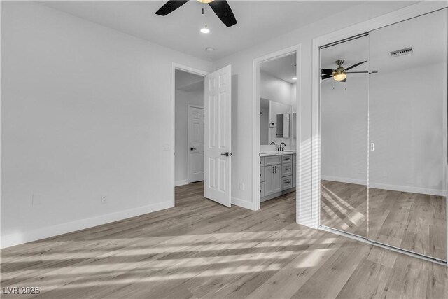 unfurnished bedroom with connected bathroom, a closet, light hardwood / wood-style floors, ceiling fan, and sink