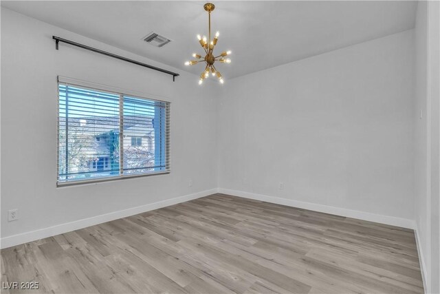 empty room featuring a notable chandelier and light wood-type flooring