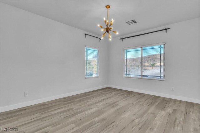 spare room featuring light wood-type flooring and a notable chandelier