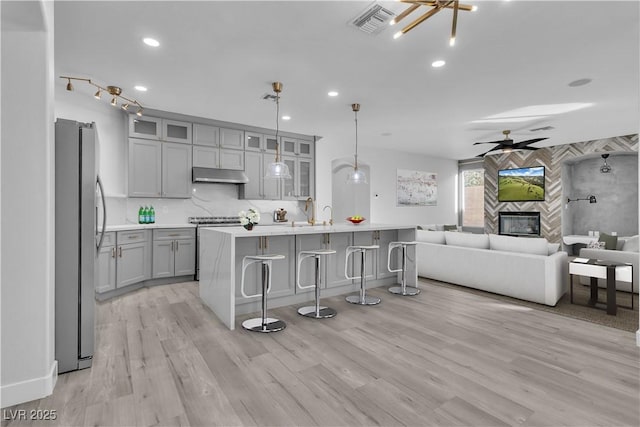 kitchen with tasteful backsplash, ceiling fan with notable chandelier, stainless steel fridge, a high end fireplace, and pendant lighting