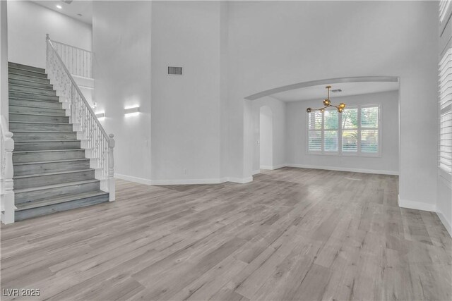 unfurnished living room with a towering ceiling, light wood-type flooring, and a chandelier