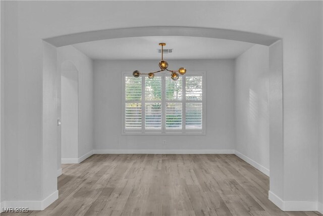 empty room featuring an inviting chandelier and light wood-type flooring