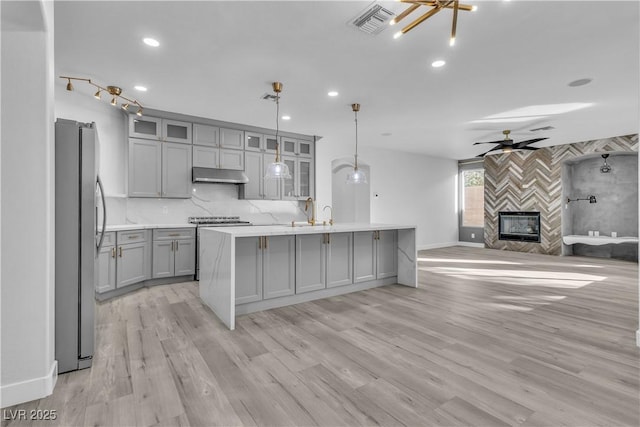 kitchen with gray cabinets, a center island with sink, ceiling fan, stainless steel fridge, and pendant lighting