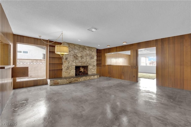 unfurnished living room with concrete flooring, a stone fireplace, a textured ceiling, and wood walls