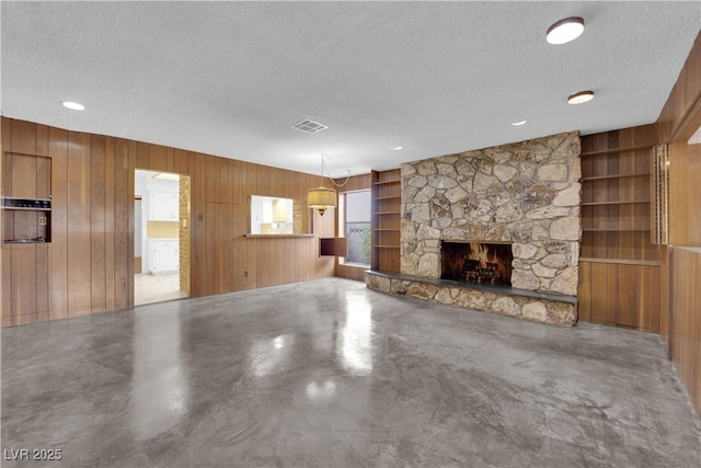 unfurnished living room featuring wooden walls, a fireplace, a textured ceiling, built in shelves, and concrete floors