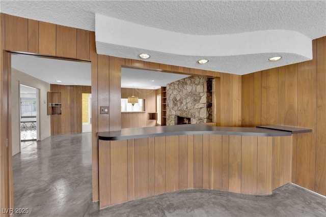 kitchen featuring a stone fireplace, a textured ceiling, wood walls, and concrete flooring