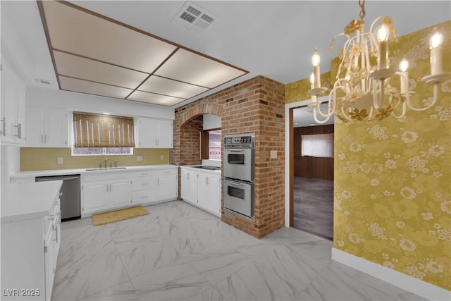 kitchen featuring appliances with stainless steel finishes, decorative backsplash, white cabinets, decorative light fixtures, and sink