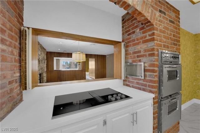 kitchen with brick wall, white cabinets, hanging light fixtures, stainless steel double oven, and black electric cooktop