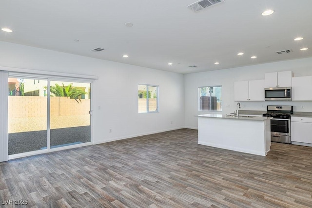 kitchen with a center island with sink, white cabinets, light hardwood / wood-style flooring, and appliances with stainless steel finishes