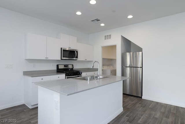 kitchen with stainless steel appliances, washing machine and dryer, a kitchen island with sink, white cabinetry, and sink