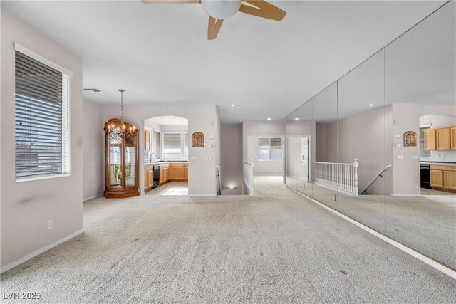 unfurnished living room featuring ceiling fan with notable chandelier and light carpet