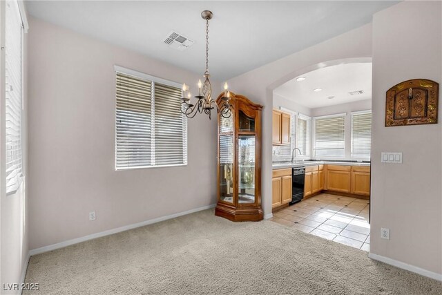 kitchen with pendant lighting, light brown cabinetry, black dishwasher, light colored carpet, and a notable chandelier