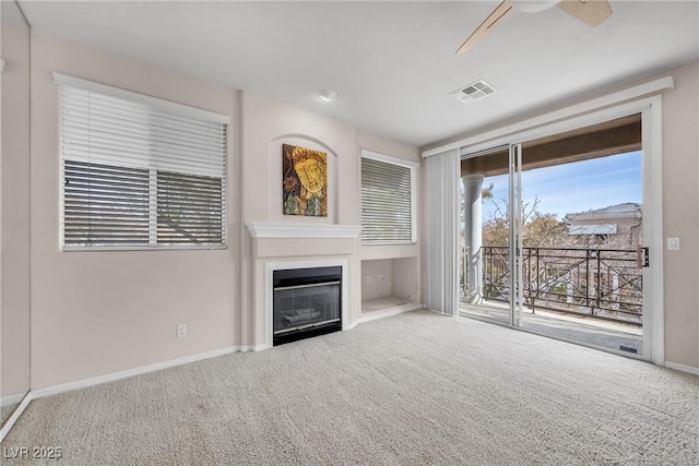 unfurnished living room with visible vents, baseboards, carpet flooring, a glass covered fireplace, and a ceiling fan