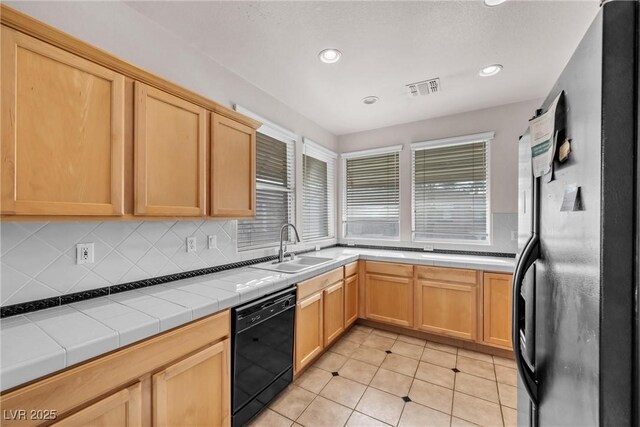 kitchen featuring sink, tasteful backsplash, refrigerator, tile counters, and black dishwasher