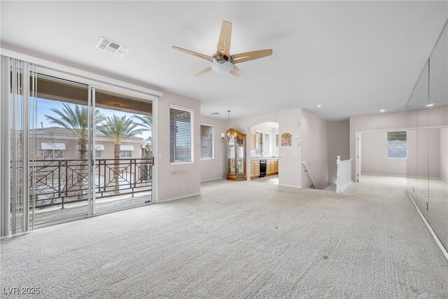 unfurnished living room featuring ceiling fan with notable chandelier, light colored carpet, and a healthy amount of sunlight