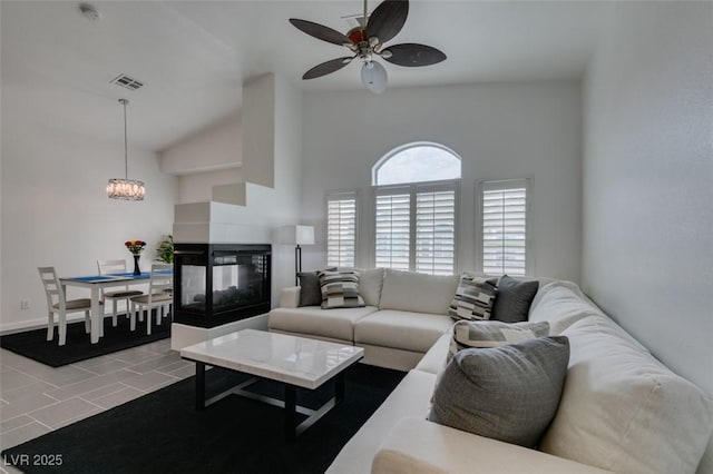 tiled living room with ceiling fan with notable chandelier, a multi sided fireplace, and lofted ceiling