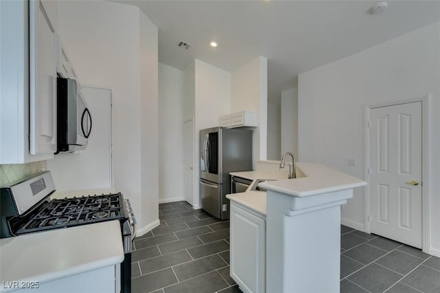 kitchen with kitchen peninsula, dark tile patterned floors, white cabinetry, appliances with stainless steel finishes, and sink