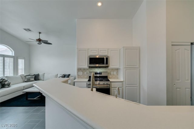 kitchen with stainless steel appliances, white cabinets, ceiling fan, decorative backsplash, and dark tile patterned floors