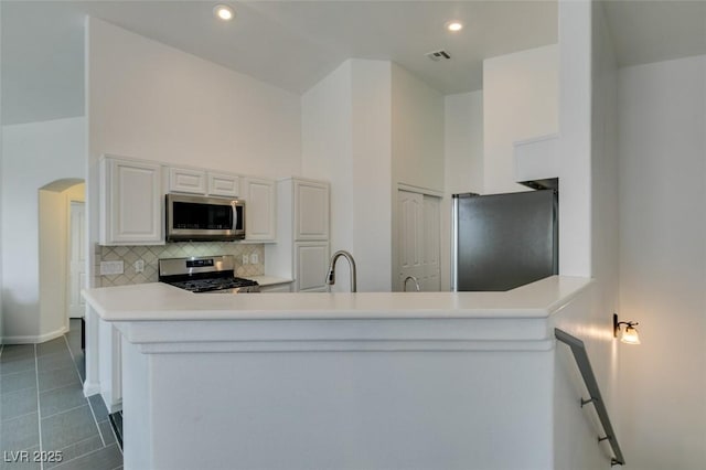 kitchen with white cabinets, kitchen peninsula, decorative backsplash, a high ceiling, and appliances with stainless steel finishes