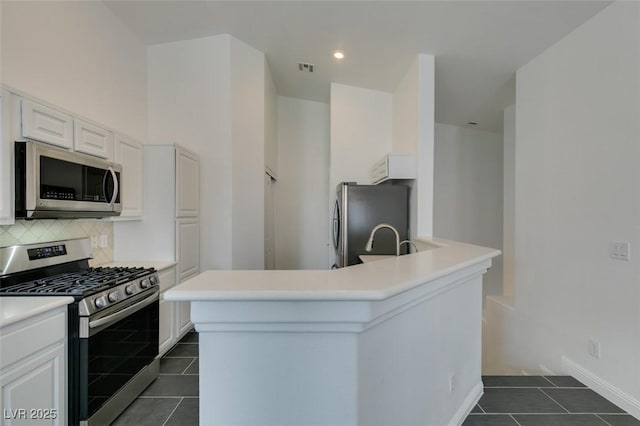 kitchen featuring appliances with stainless steel finishes, an island with sink, dark tile patterned floors, white cabinetry, and backsplash