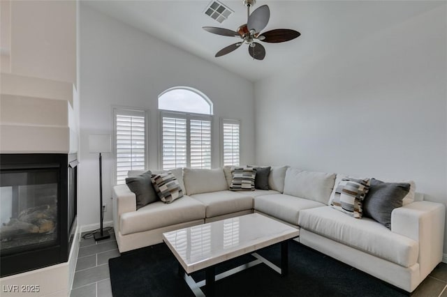 living room with ceiling fan, a multi sided fireplace, high vaulted ceiling, and tile patterned floors