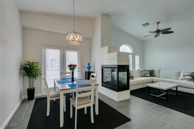 dining space featuring ceiling fan with notable chandelier, high vaulted ceiling, a tile fireplace, and tile patterned flooring