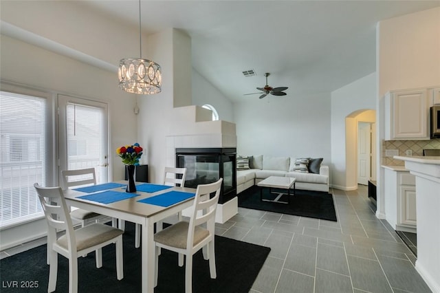 dining room with ceiling fan with notable chandelier, a tile fireplace, and light tile patterned floors