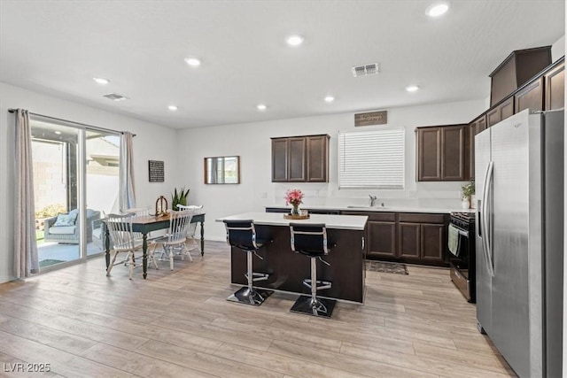 kitchen featuring gas stove, a kitchen bar, light hardwood / wood-style flooring, stainless steel refrigerator with ice dispenser, and a kitchen island