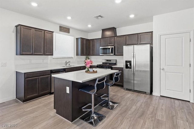 kitchen featuring stainless steel appliances, light hardwood / wood-style floors, a kitchen bar, a kitchen island, and sink