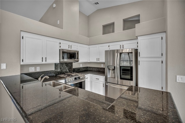 kitchen featuring dark stone countertops, appliances with stainless steel finishes, white cabinets, lofted ceiling, and sink