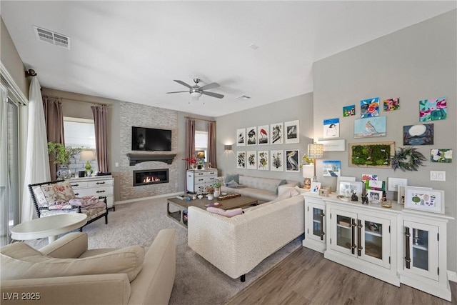 living room featuring a large fireplace, ceiling fan, plenty of natural light, and hardwood / wood-style flooring